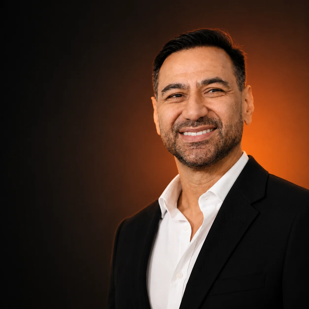 Andre Magrini smiling in a black jacket against a warm orange studio background