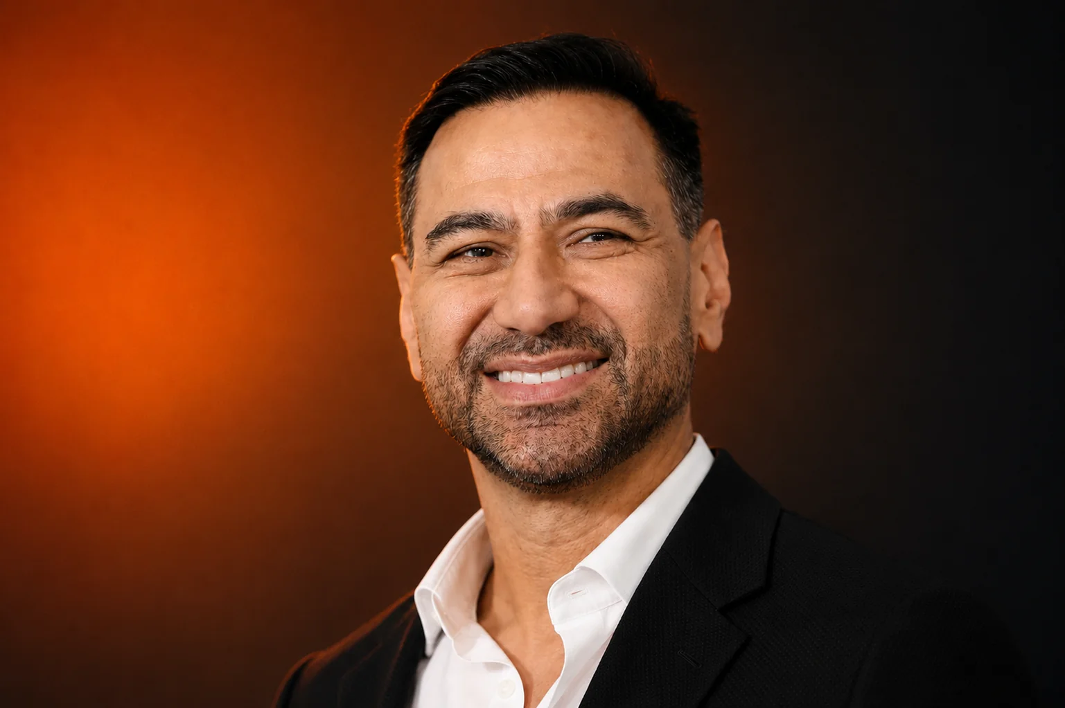 Andre Magrini executive portrait in a black jacket against a warm orange studio background